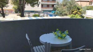 Un balcon avec une table et des chaises, un vase décoratif et une vue sur un immeuble doté d’un balcon.