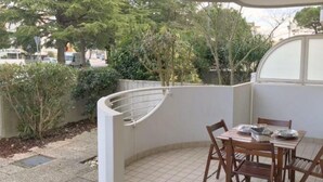 Un piccolo patio con tavolo e sedie, circondato da un muro bianco e una ringhiera curva.