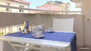 En balkong med ett bord dukat för två personer, med en kaffebryggare, koppar och fat.