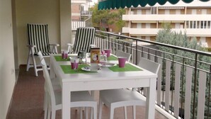 Un balcon avec une table et des chaises blanches, une chaise à rayures et un auvent vert.