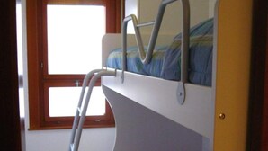 Une chambre avec un lit superposé, une fenêtre, un fauteuil roulant et une couvre-lit aux couleurs vives.