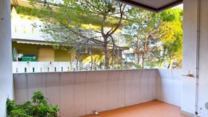 Un balcon donnant sur des arbres et des immeubles, une plante en pot et un sol carrelé.