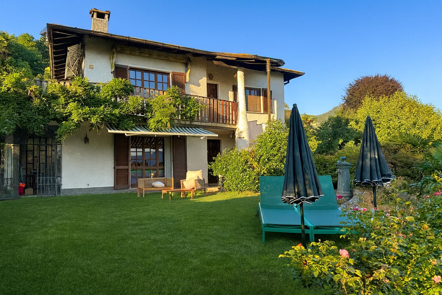 Una casa de dues plantes amb un balcó, un jardí i mobiliari d'exterior.