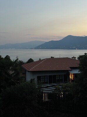 A house with a red roof, a wooden fence, and a view of a body of water and mountains in the background. - Above the Lake (Colmegna)