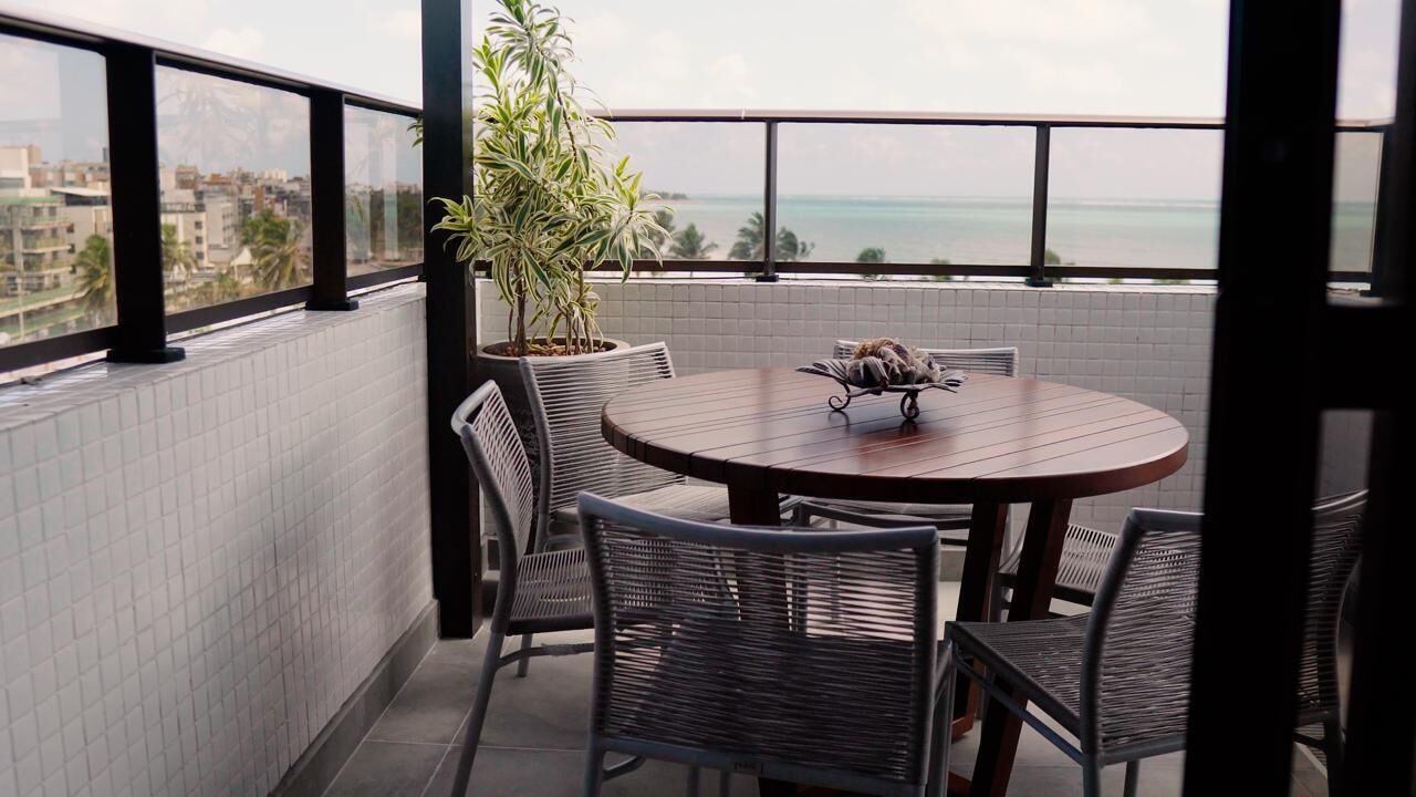 Un balcon avec une table ronde et des chaises, une plante en pot et une vue sur la mer.