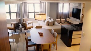 Ein modernes Hotelzimmer mit Essbereich, Sofa, Fernseher und Küchenzeile.