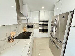 Une cuisine compacte avec des meubles blancs, une plaque de cuisson à induction noire, un four à micro-ondes, un four double et un réfrigérateur en acier inoxydable.