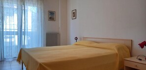 A bedroom with a bed, a nightstand, a radiator, and a window with sheer curtains. - Family friendly vacation apartment with a balcony (Grado)