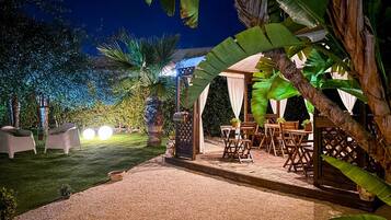 Un espace extérieur aménagé en terrasse, avec des tables et des chaises, entouré d’une végétation luxuriante et de palmiers.