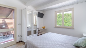 Ein Schlafzimmer mit einem Bett, einem an der Wand montierten Fernseher, einem Fenster und einer Tür zu einem Außenbereich.