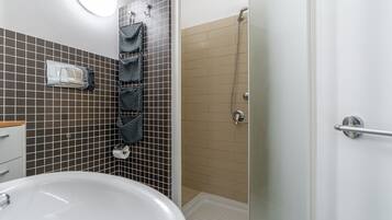 Une salle de bain avec un lavabo blanc, une cabine de douche en verre et un porte-serviettes avec plusieurs serviettes.