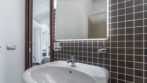 Ein Badezimmer mit einem weißen Waschbecken, dunklen Fliesenwänden und einem Spiegel.