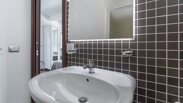 Une salle de bain avec un lavabo blanc, des murs recouverts de carreaux foncés et un miroir.