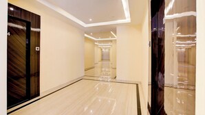A modern hotel corridor with a polished floor, recessed lighting, and a wooden door on the left. - Hotel Saffron Suites (Chaibasa)