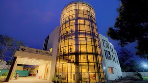 A modern hotel with a cylindrical glass facade, a welcoming sign, and a well-lit entrance. - Hotel Saffron Suites (Chaibasa)
