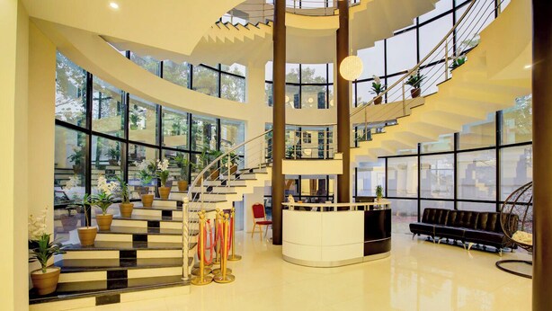 A spacious lobby with a central staircase, a reception desk, and seating area. - Hotel Saffron Suites (Chaibasa)