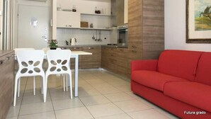 Una cocina moderna con armarios blancos, un sofá rojo y una zona de comedor con sillas blancas.