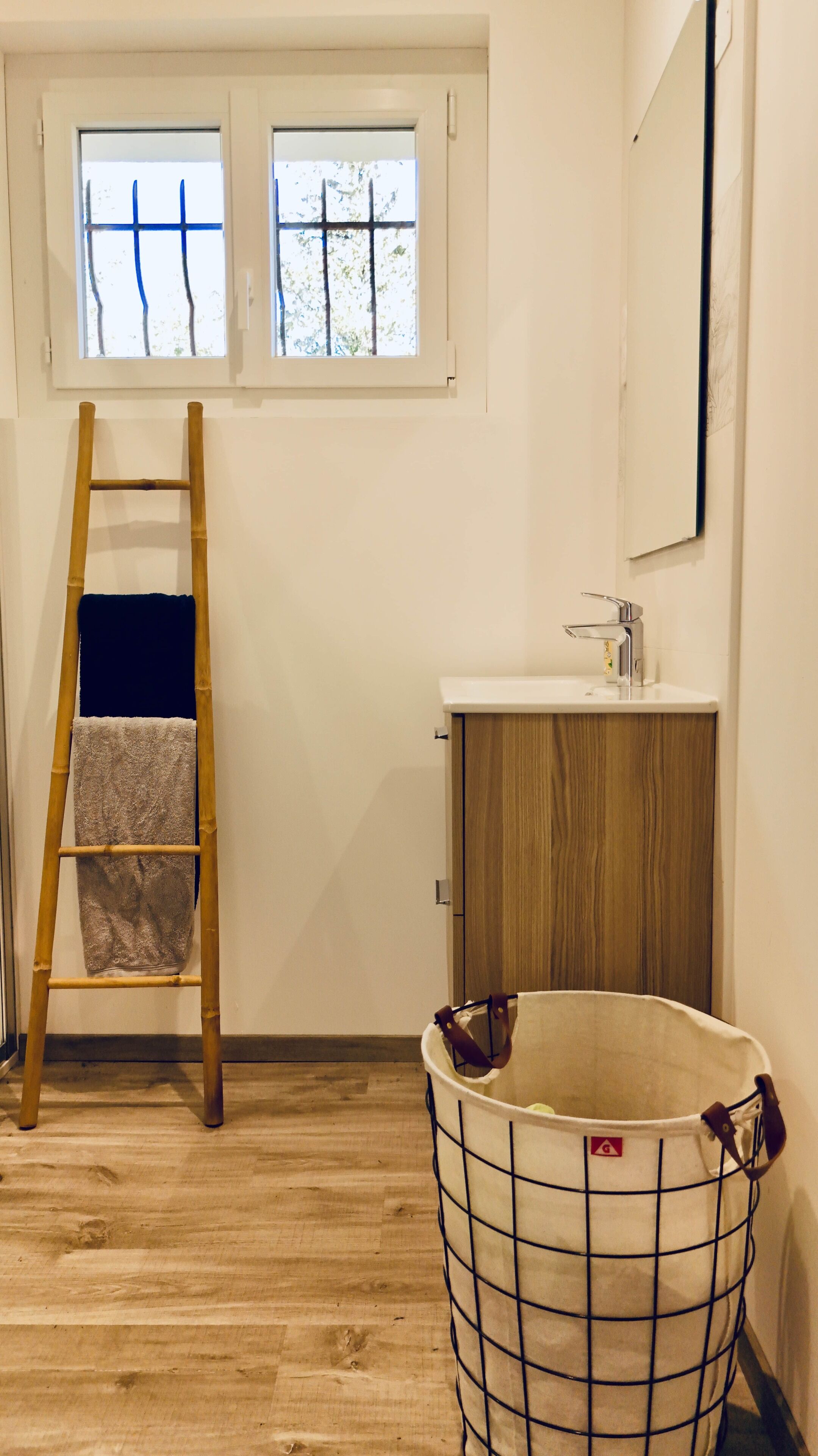 Ein Zimmer mit Holzboden, einer Holzleiter, einem weißen Eimer, einem Holzkasten und einem Fenster mit Blick auf Bäume.