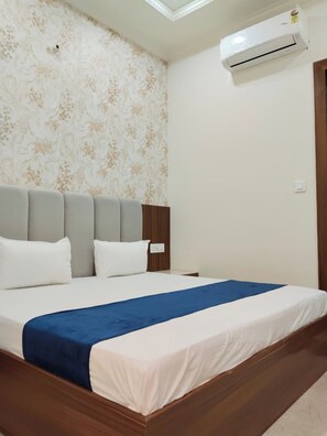 Un dormitorio con cama, mesita de noche, aire acondicionado instalado en la pared y papel tapiz estampado.