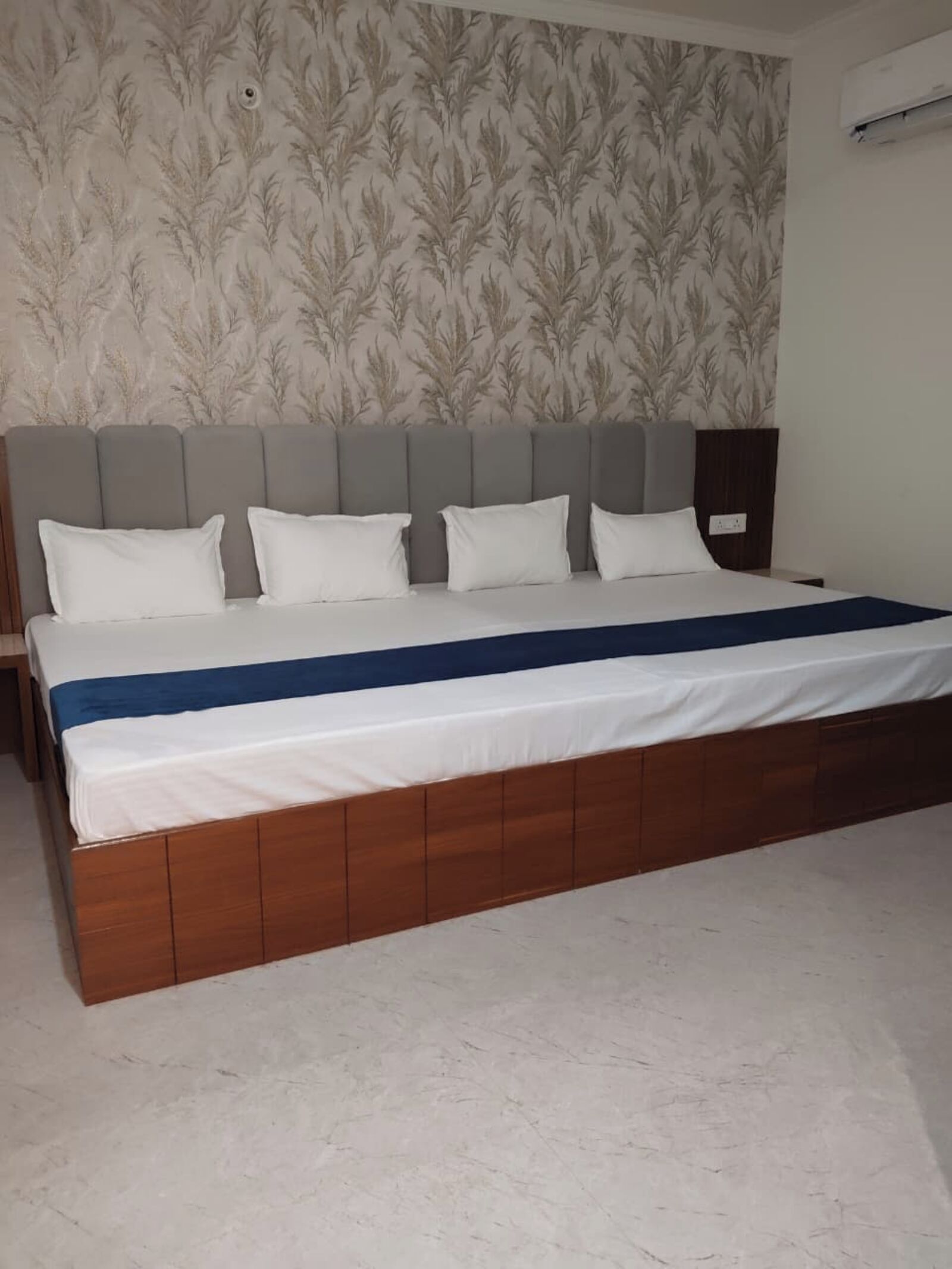 A bed with a wooden frame and white bedding, a grey headboard, and a patterned wallpaper background.
