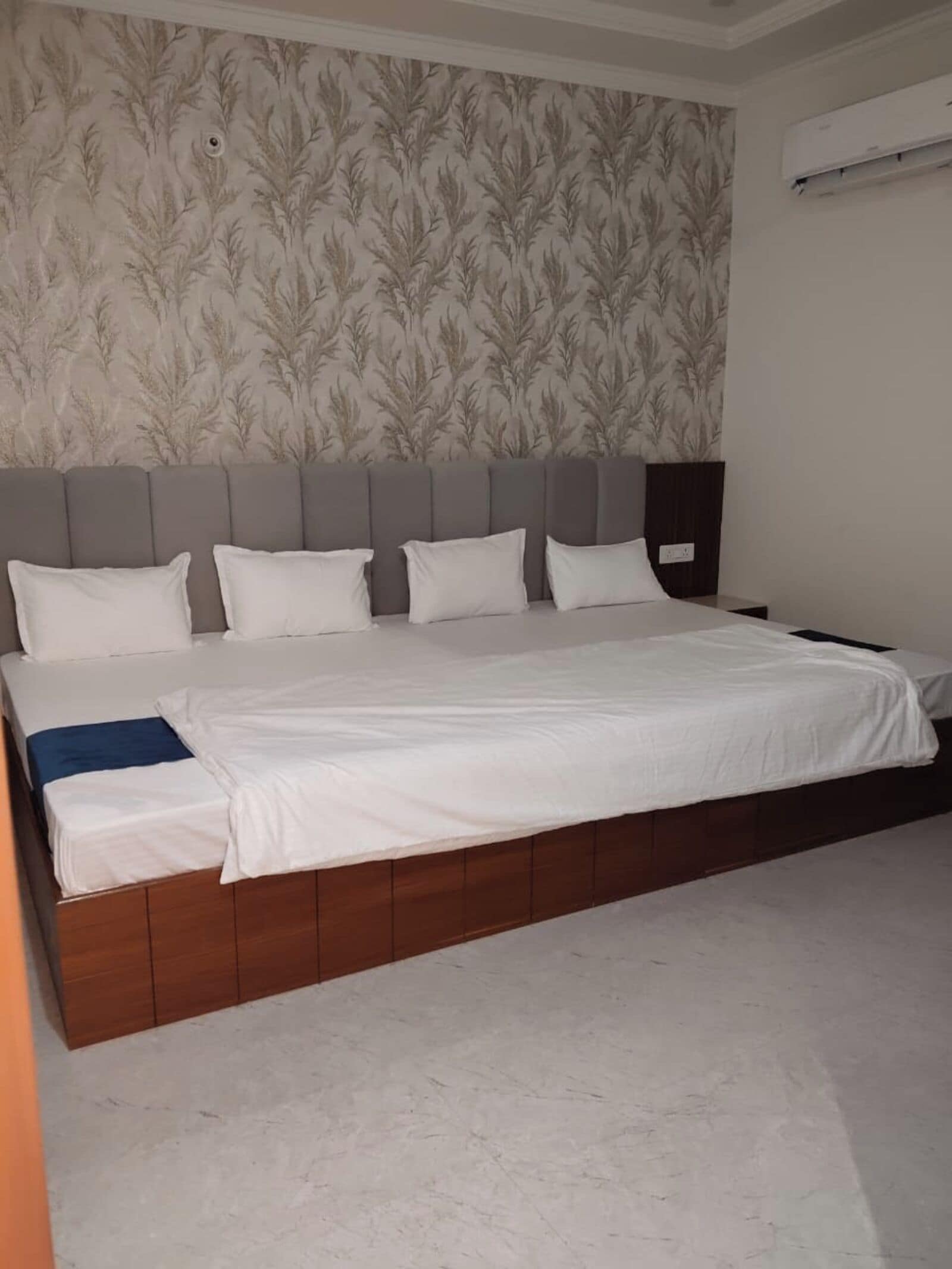 Una cama grande con cabecera de madera, ropa de cama blanca y un papel tapiz estampado.