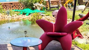 Una silla roja y una mesa de vidrio en una terraza de madera con vista a una playa y un estanque.