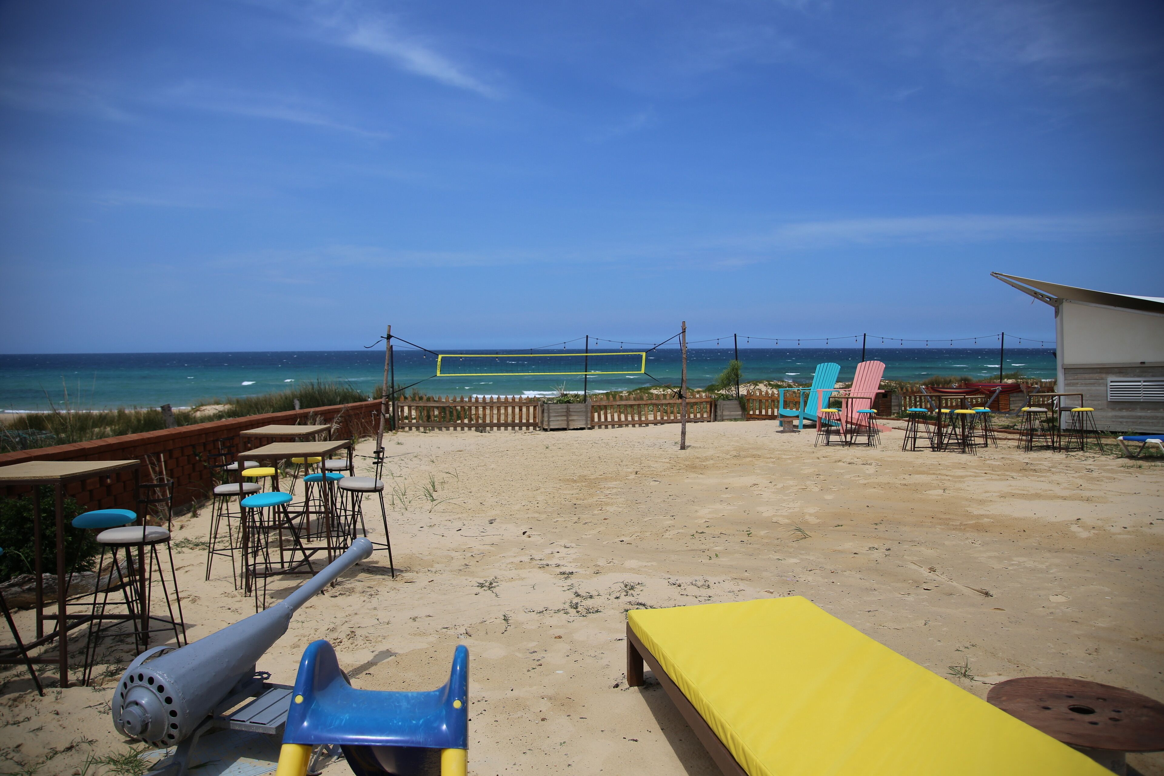 A beachside patio with tables and chairs, a yellow sofa, and a cannon.