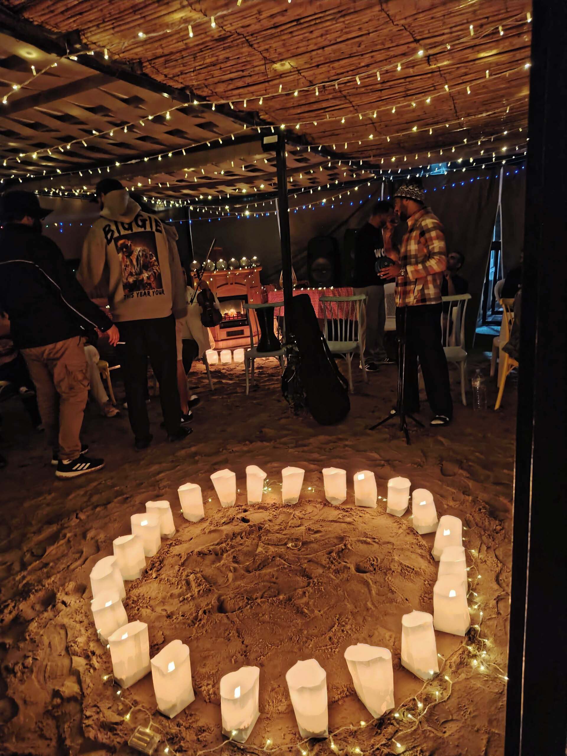 A rustic venue with a wooden ceiling, string lights, and a central fire pit surrounded by candles.