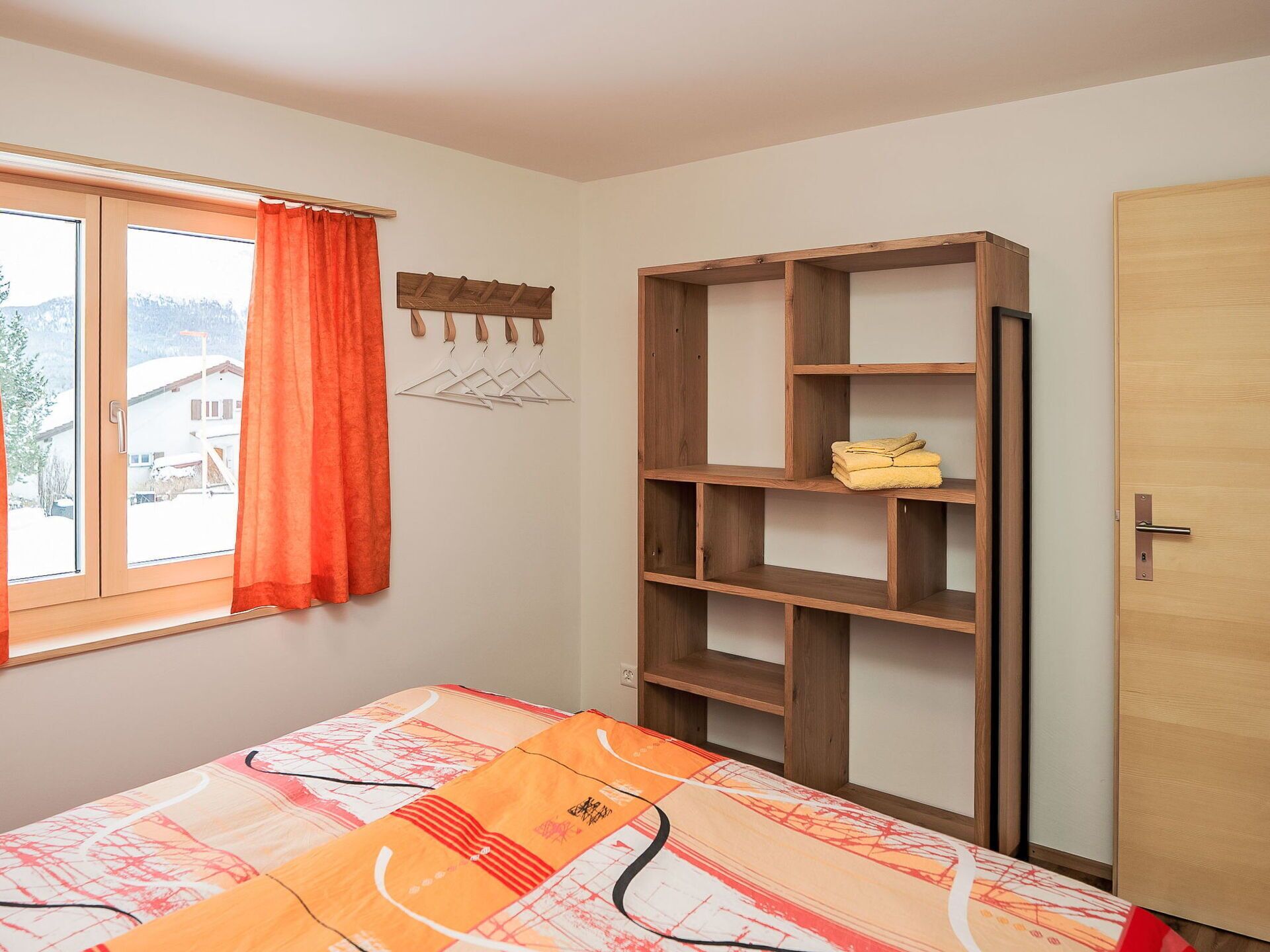 A bedroom with a bed, a wooden wardrobe, a window with curtains, and a view of a snowy landscape.