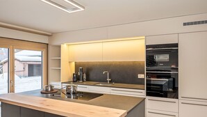 A modern kitchen with a central island, built-in appliances, and a view of a snowy landscape through the glass door. - Nice apartment for 4 guests with WIFI and TV (Samedan)
