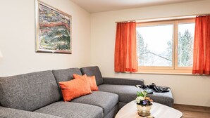 A modern living room with a grey sofa, an orange cushion, a coffee table with a flower vase, and a painting on the wall. - Nice apartment for 4 guests with WIFI and TV (Samedan)