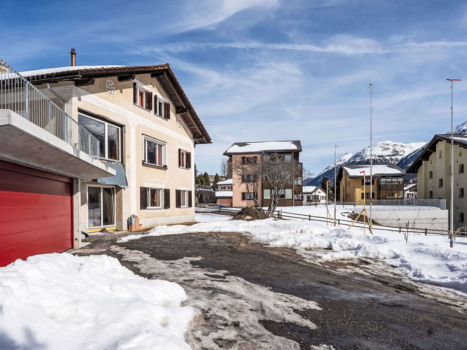 Ein Wohngebiet mit Häusern, einer roten Garage und einer verschneiten Landschaft mit Bergen im Hintergrund.