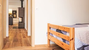 A bedroom with a wooden bed, a kitchen in the background, and a hallway leading to an open space. - Nice apartment for 4 guests with WIFI and TV (Samedan)