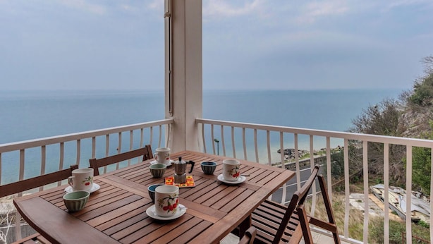 Ein Holztisch mit Tassen und einem Teekessel auf einem Balkon mit Blick aufs Meer.
