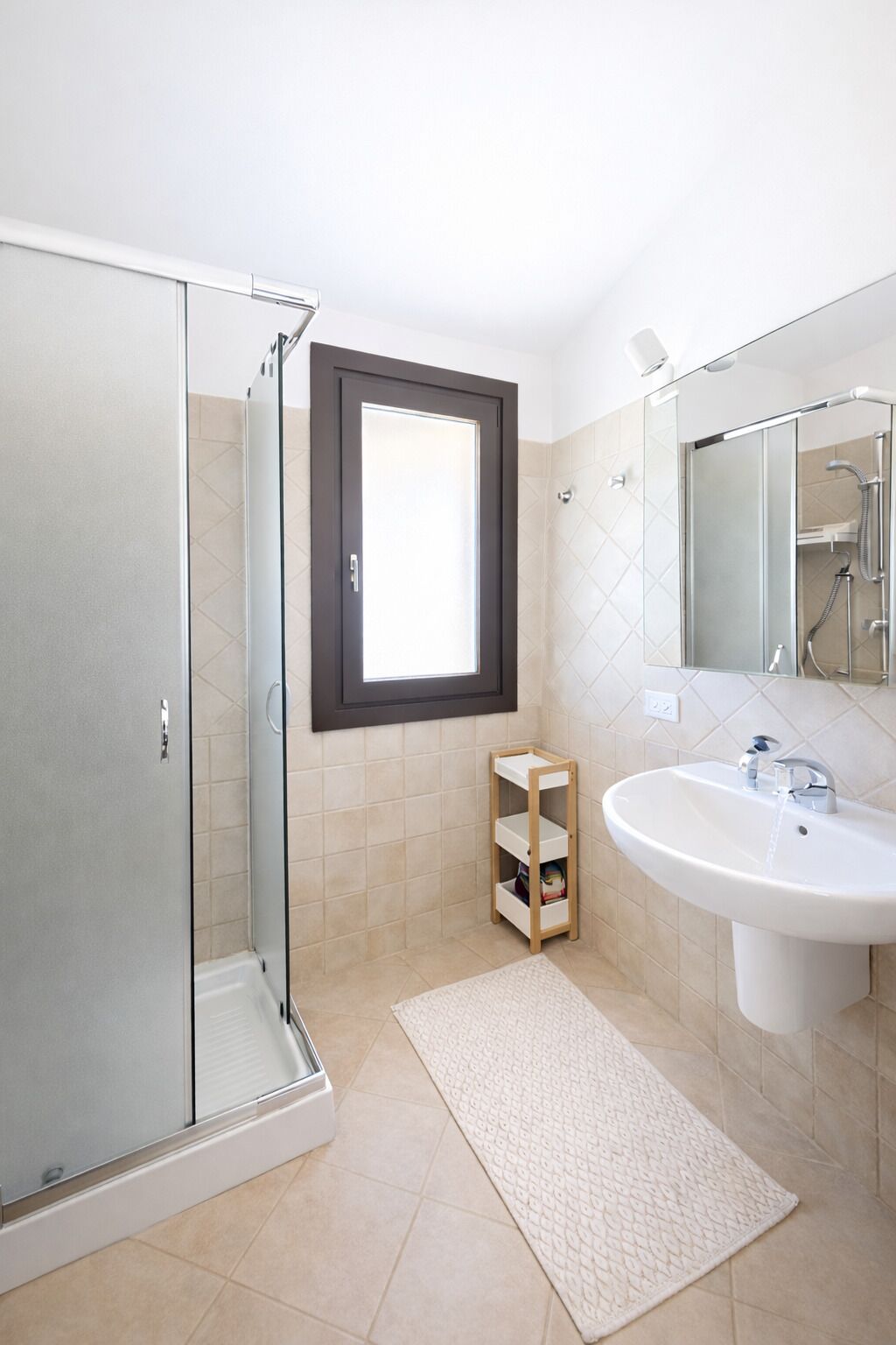 A modern bathroom with a glass shower enclosure, a white sink, and a small wooden shelf.