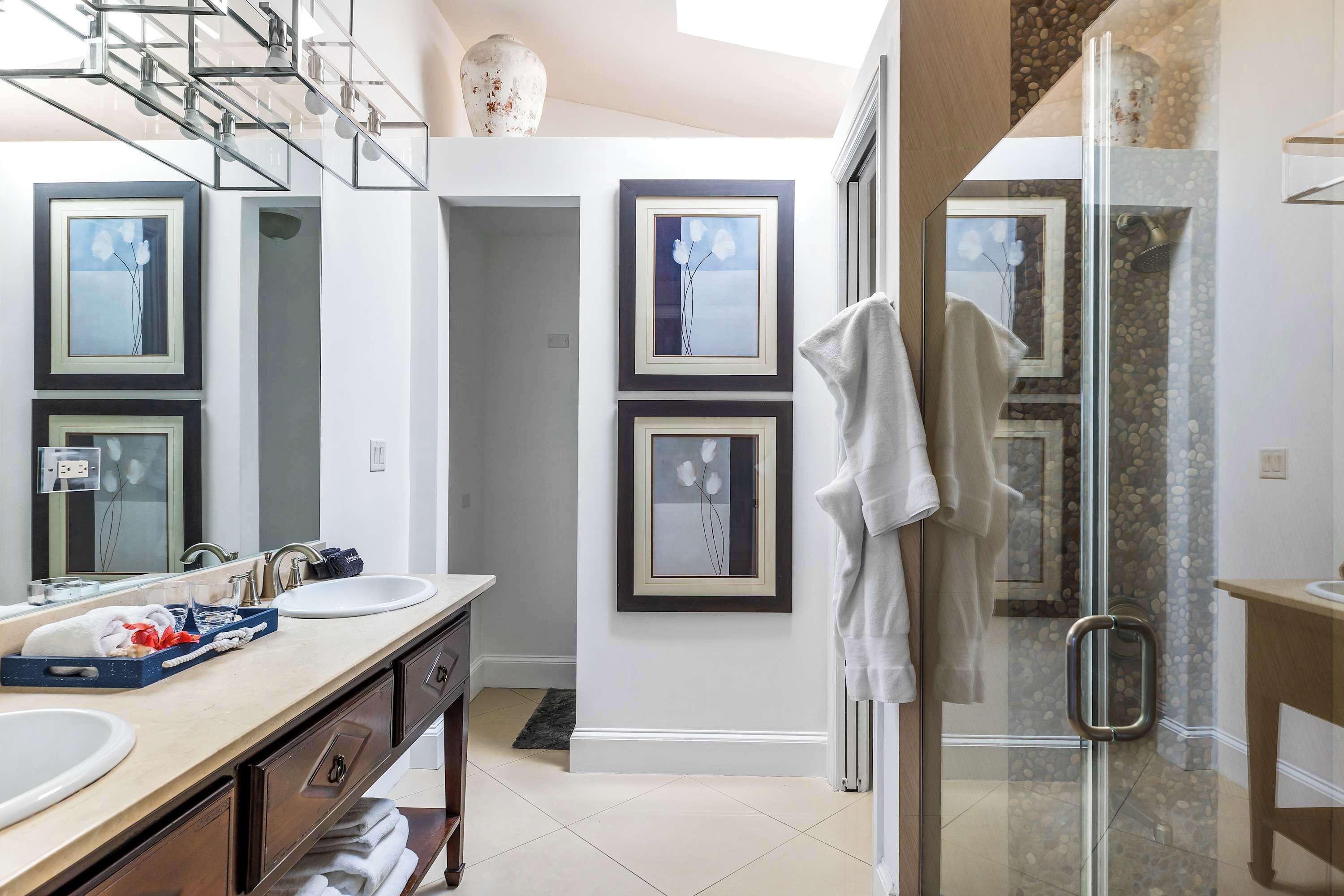 Un bagno moderno con due lavandini, cabina doccia in vetro e opere d'arte incorniciate alle pareti.
