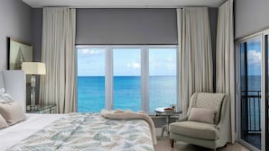 Ein Hotelzimmer mit einem großen Bett, einem Sessel, einem kleinen Tisch und Meerblick durch große Fenster.