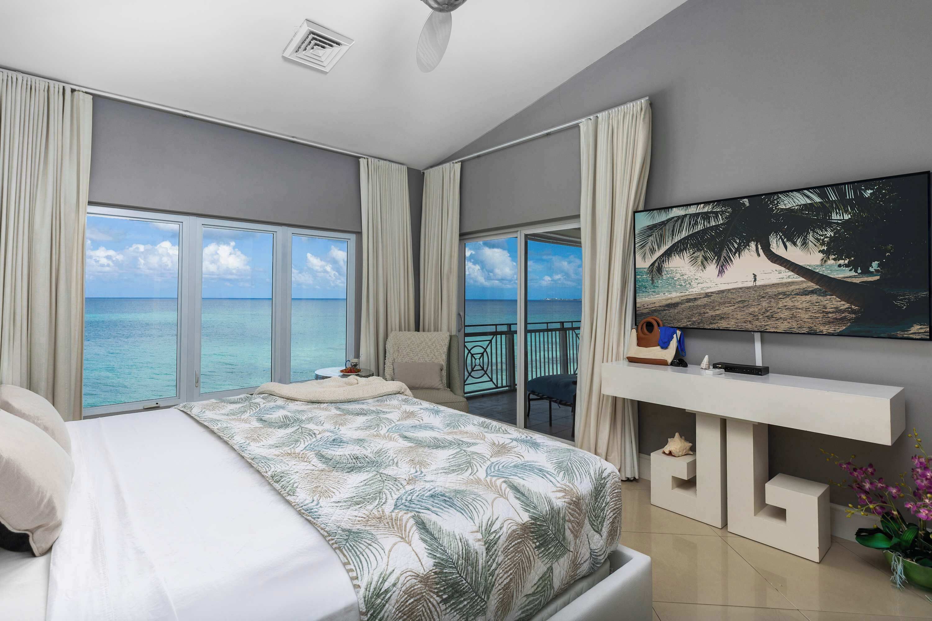 Un dormitorio con una cama grande, televisión y un balcón con vista al mar.