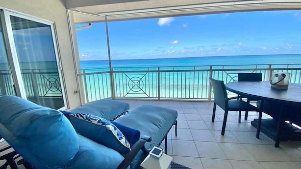 Ein Balkon mit Blick auf das Meer, einem Esstisch und blauen Sitzmöbeln.