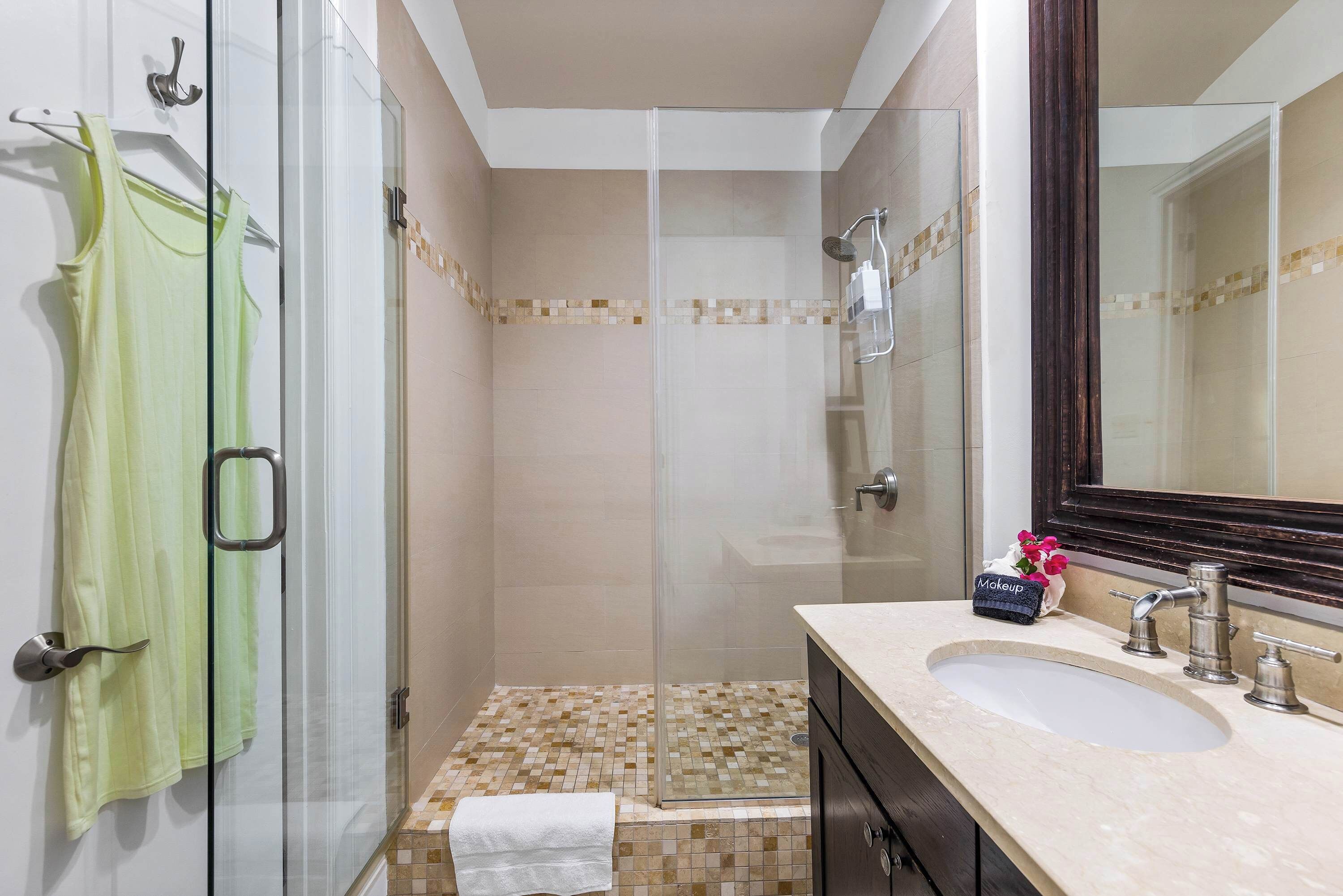 Un baño con cabina de ducha de vidrio, lavamanos con espejo y toallero con una toalla verde.