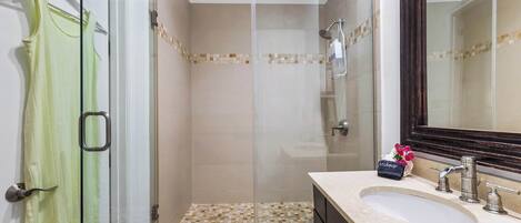 Un baño con cabina de ducha de vidrio, lavamanos con espejo y toallero con una toalla verde.