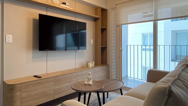 A modern living room with a flat-screen TV mounted on the wall, a wooden cabinet below, a round coffee table with a decorative item, and a sofa. - w Marvelous 2BR w Balcony in Miraflores (Lima)
