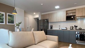 A modern living room with a beige sofa, a round wooden coffee table, and a kitchen area with grey cabinets and stainless steel appliances. - w Marvelous 2BR w Balcony in Miraflores (Lima)