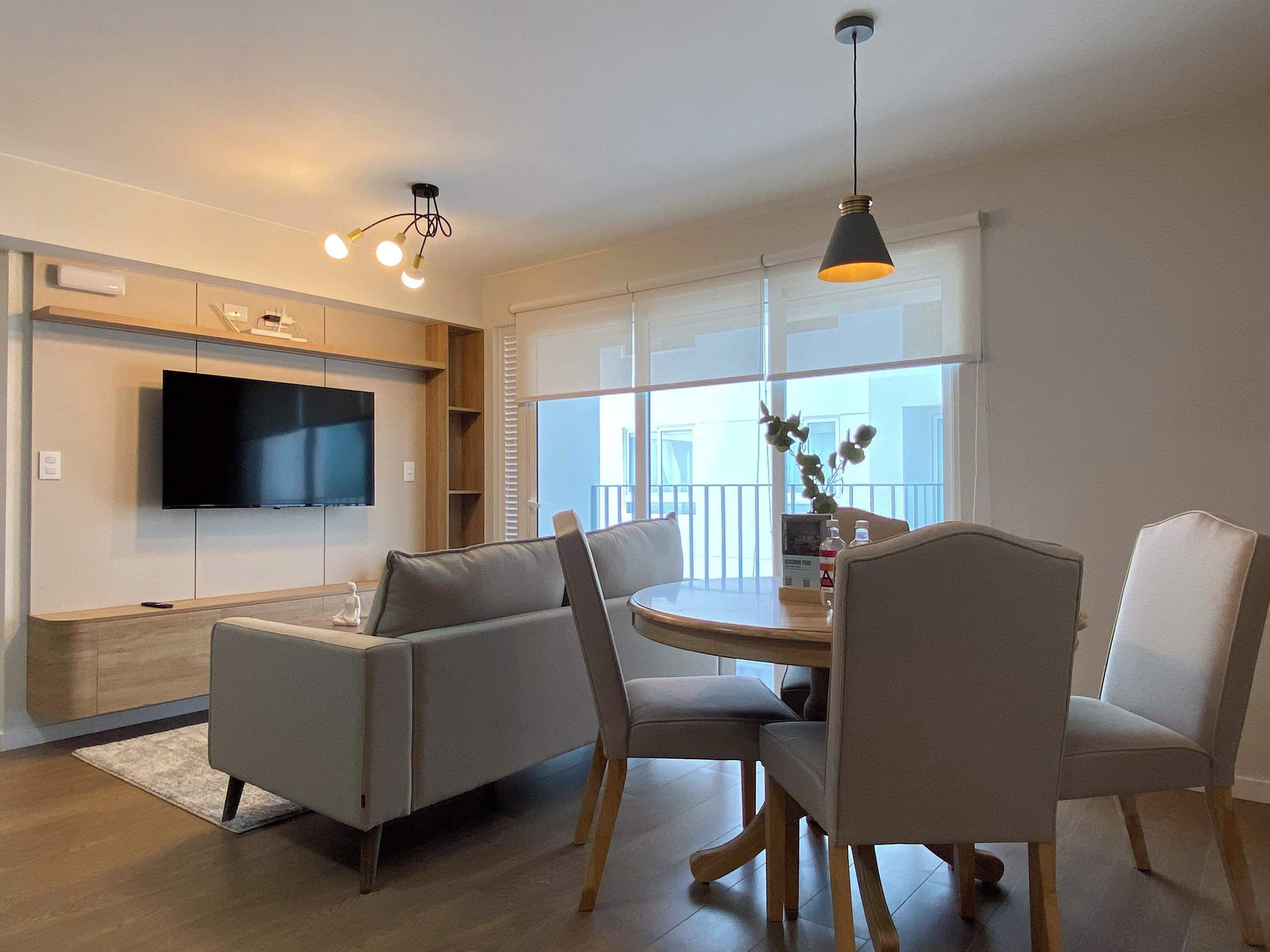 A modern living room with a flat-screen TV, a dining table with chairs, and a sofa.