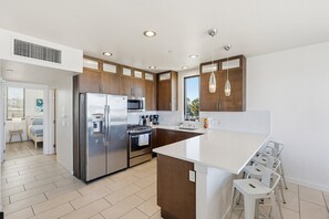 A modern kitchen with stainless steel appliances, wooden cabinets, and a large island with bar stools. - 6BR/6BA Luxury Group-Friendly (San Diego)