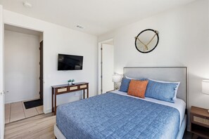 Ein Schlafzimmer mit einem Bett, einem Fernseher, einem Nachttisch, einer Lampe und einem Spiegel an der Wand.