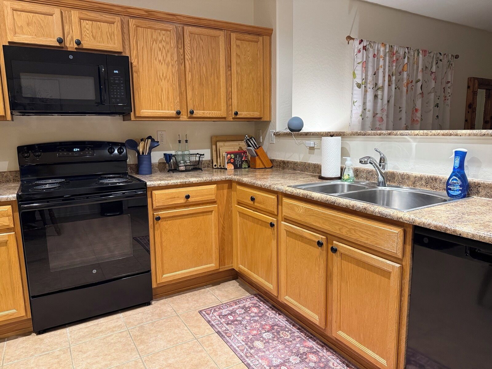 A kitchen with wooden cabinets, a black stove, a microwave, and a sink.