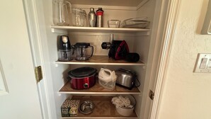 Una despensa de cocina con estantes que contienen diversos electrodomésticos y recipientes de almacenamiento.