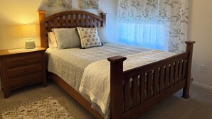 Un dormitorio con cama de madera, una mesita de noche, una lámpara y una ventana con cortinas.