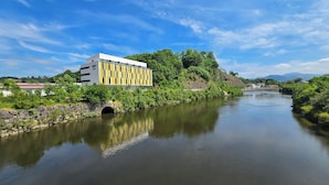 Ein Fluss mit einer Steinbrücke, ein Gebäude mit gelb-weißer Fassade und Grün im Hintergrund.